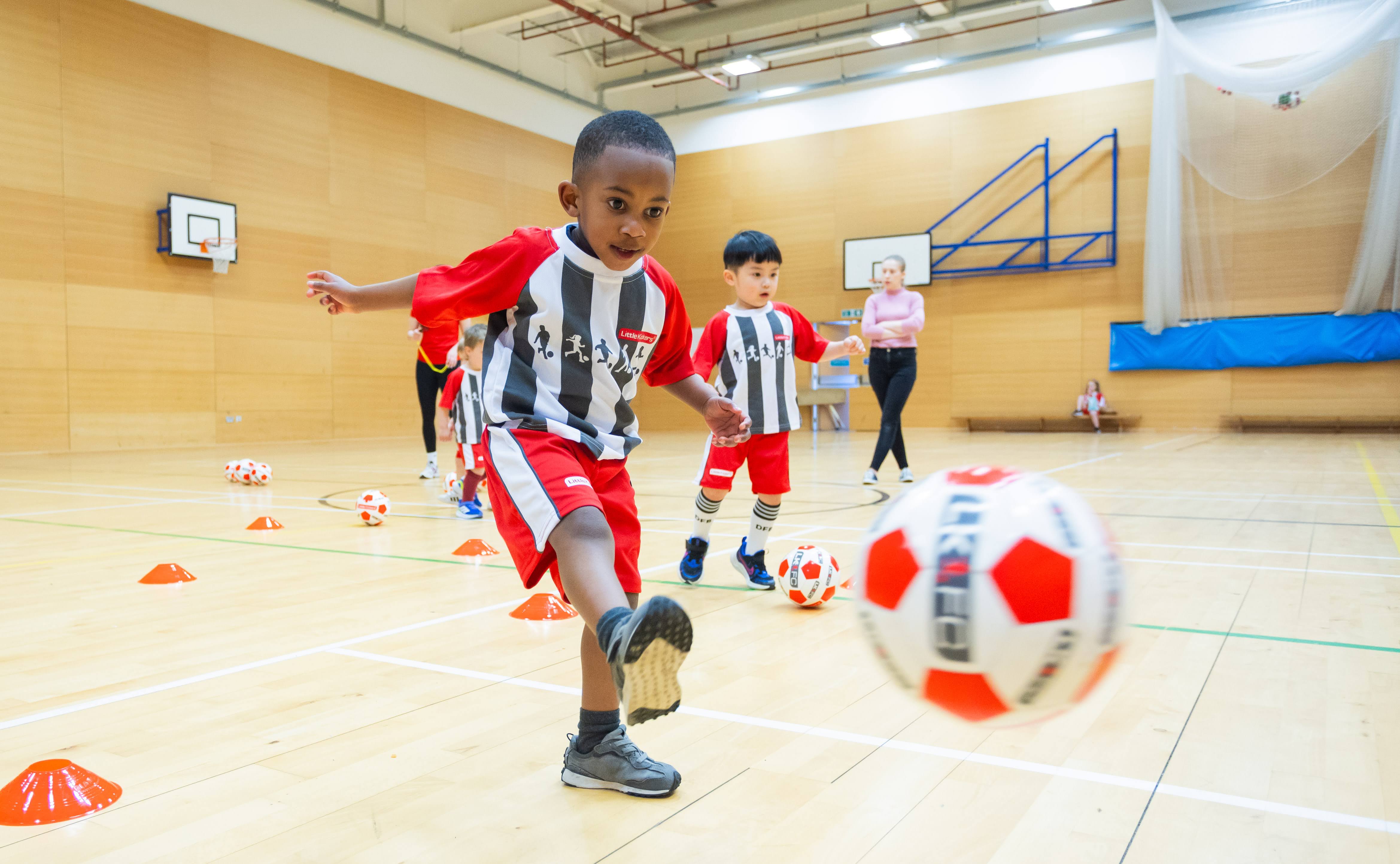 Young Little Kickers player in red and white kit kicking a football
